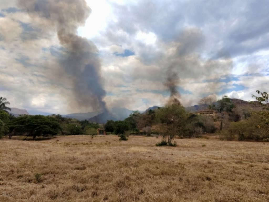 Grandes columnas de humo se elevan desde la zona montañosa y son visibles desde un terreno abierto cercano a la emergencia.